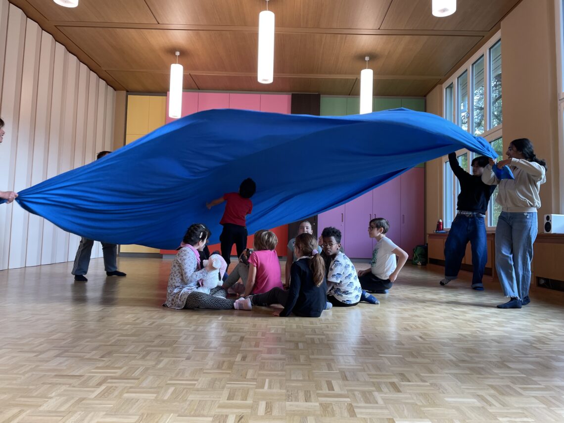 Mehrere Kinder sitzen auf dem Boden, über ihnen ist ein grosses Tuch