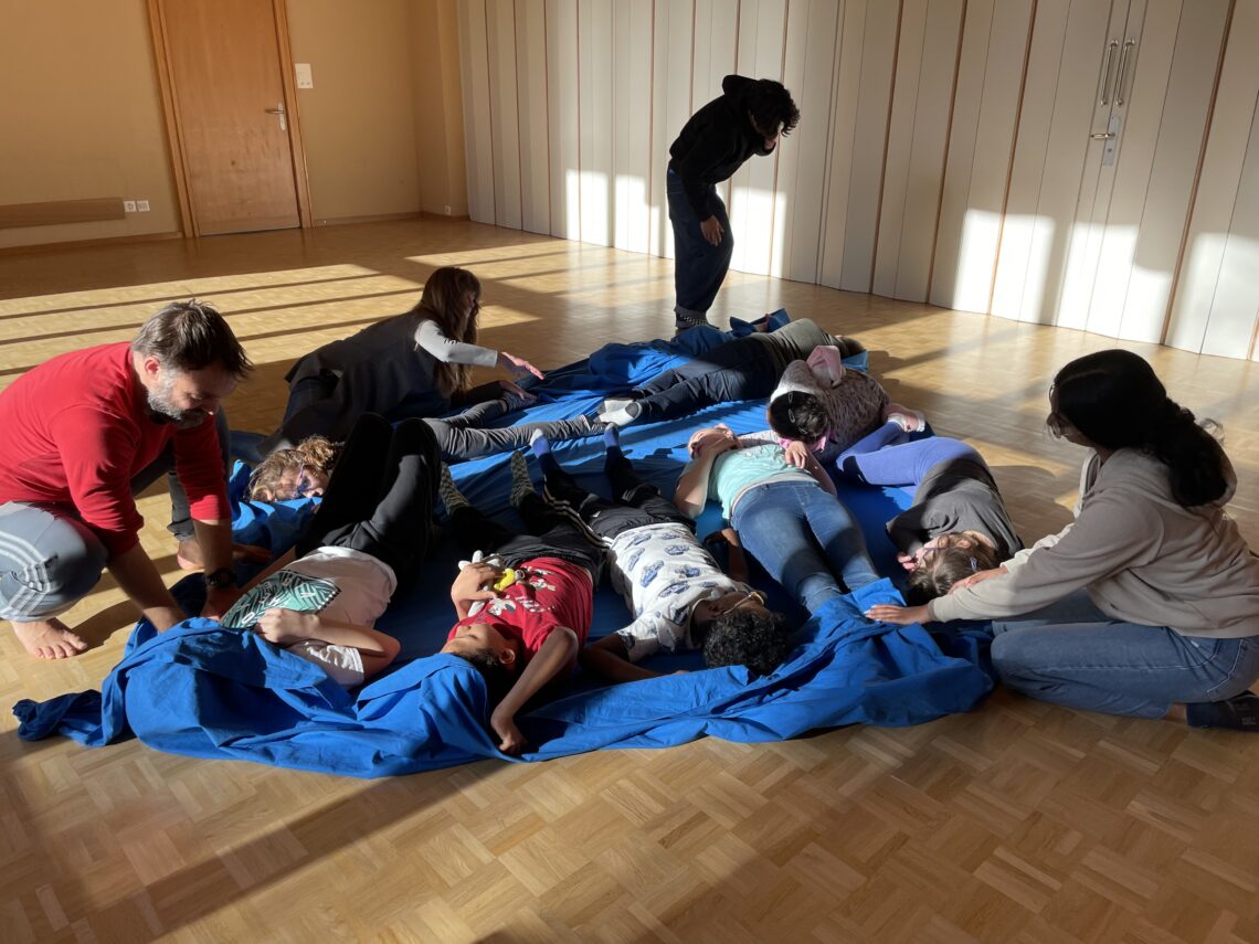Mehrere Kinder liegen durcheinander auf einem Tuch auf dem Boden